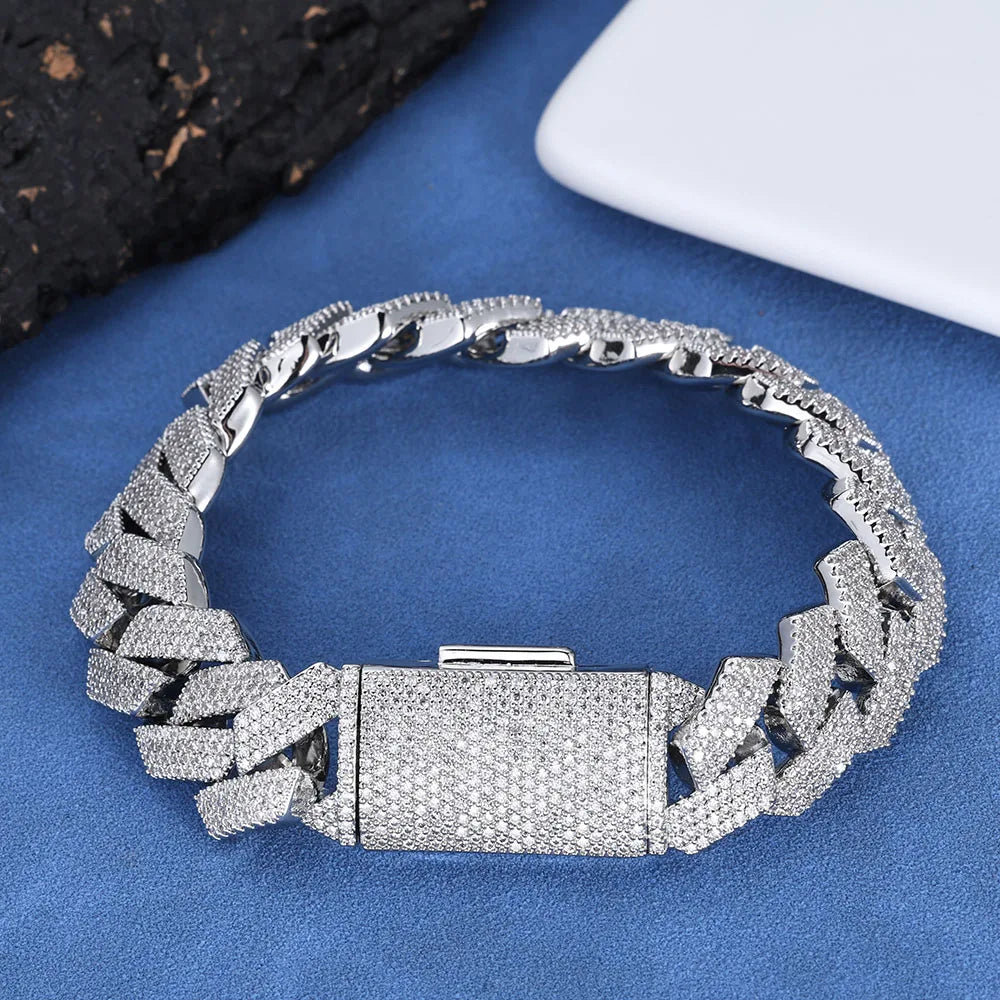 A silver-toned chain bracelet covered in small clear stones, displayed on a blue textured surface with dark and white props in the corners.