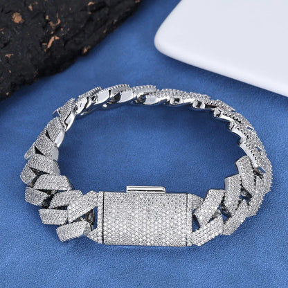 A silver-toned chain bracelet covered in small clear stones, displayed on a blue textured surface with dark and white props in the corners.